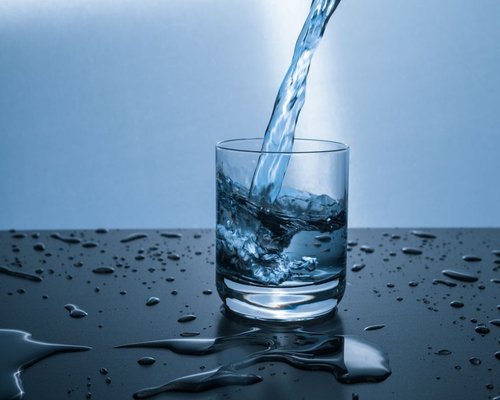 Fresh clear water pouring into a clean transparent glass on a table