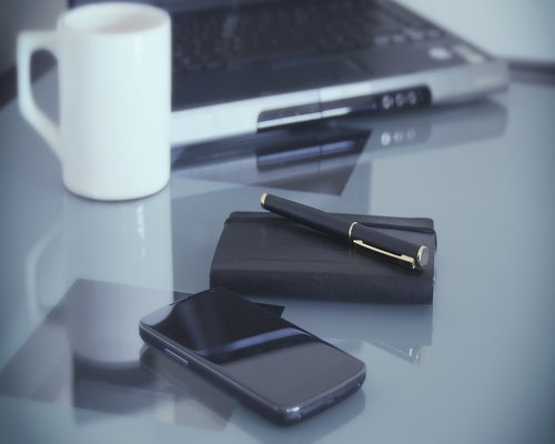 A laptop on a clean desk next to a notebook and a coffee mug in soft lighting
